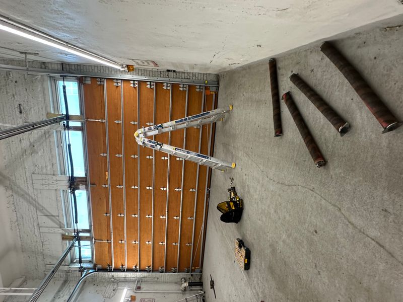 Commercial wood overhead door interior being serviced with ladder and old springs visible